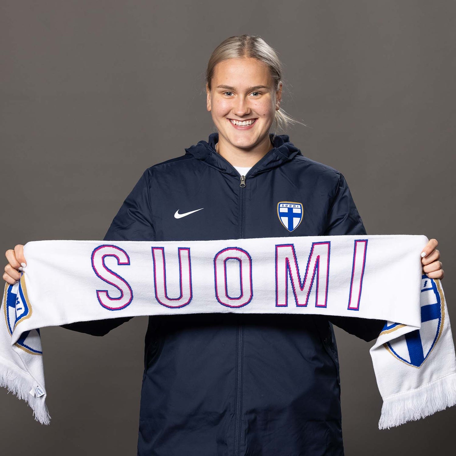 Suomi-kaulahuivi. Kudotun kannattajakaulahuivin molemmilla puolilla on pinkillä kirjailtu teksti